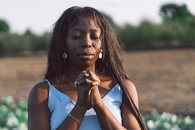 Afro girl fechou os olhos, orando ao ar livre. mãos postas em conceito de oração pela fé, espiritualidade e religião. etnia africana