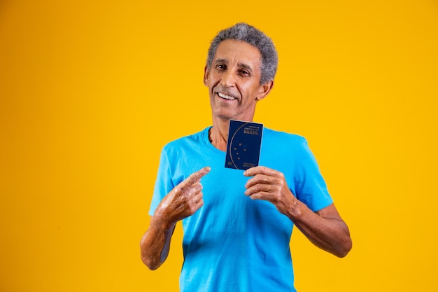 Afro idoso segurando o passaporte brasileiro nas mãos.