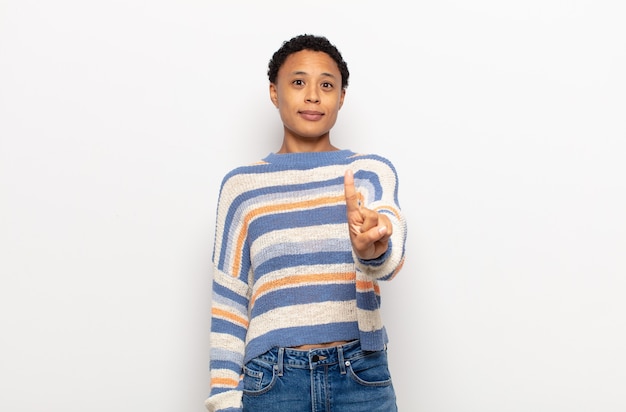 Afro joven mujer negra sonriendo con orgullo y confianza haciendo la pose número uno triunfalmente