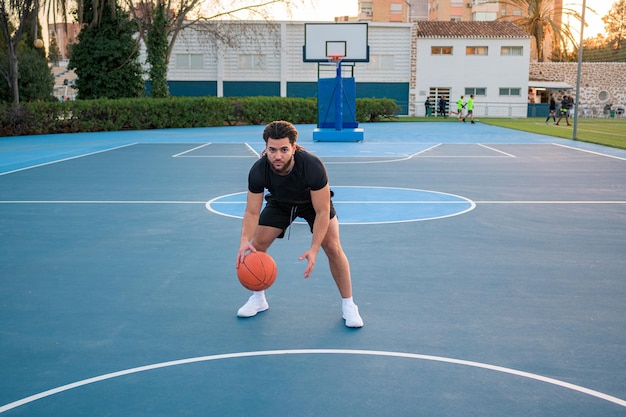 Afro-Latin-Mann, der Basketball spielt und den Ball bei Sonnenuntergang auf einem Platz hüpft