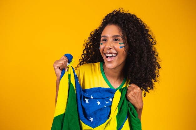 Afro-Mädchen jubeln für das brasilianische Lieblingsteam und halten die Nationalflagge in gelbem Hintergrund.