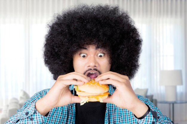 Afro-Mann isst zu Hause einen großen Cheeseburger