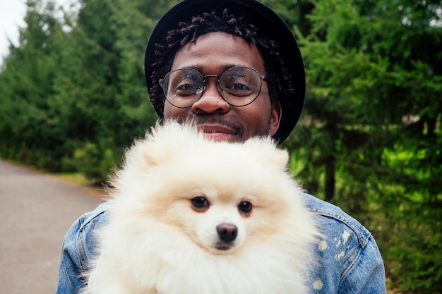 Afro-Mann umarmt seinen flauschigen Spitz im Park.