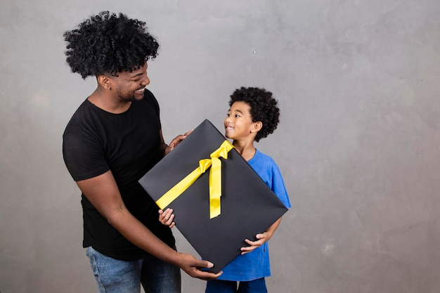 Afro padre e hijo sobre fondo neutro con espacio libre para texto con regalo