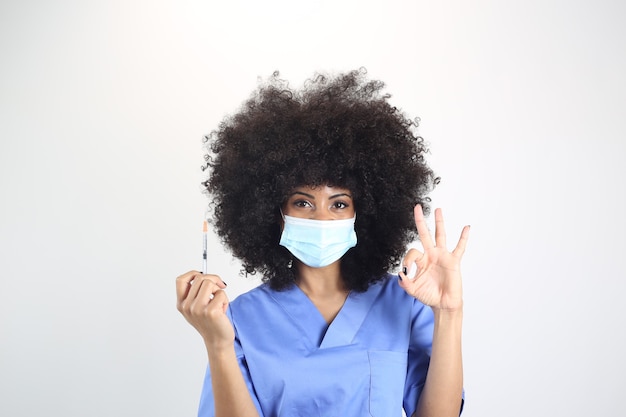 Afro-Ärztin mit medizinischer Maske und Spritze mit Impfstoff, macht eine gute Geste