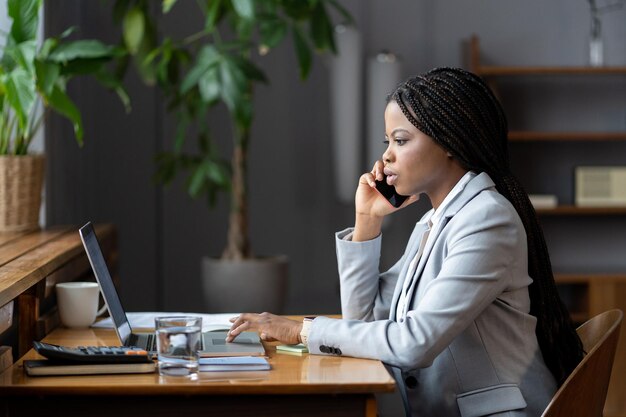 Afro-Unternehmensberaterin, die telefonisch mit dem Kunden interagiert und Daten auf dem Laptop eingibt