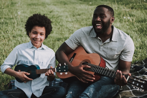 Afro-Vater und Afro-Sohn spielen auf Gitarren beim Picknick.