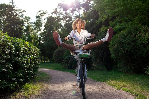 Foto afroamericana rizada chica loca monta bicicleta rápido en el parque en verano y grita