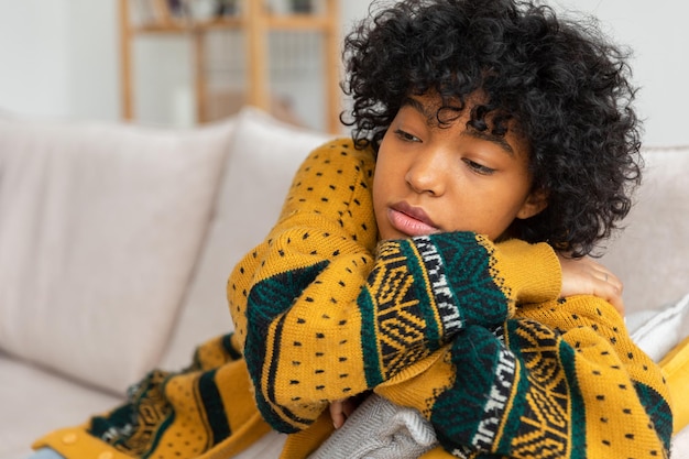 Afroamericana, triste, pensativa, pensativa, desmotivada, niña sentada en un sofá en casa interior. Una joven africana reflexiona, se ve cansada después de un largo día. La niña se siente deprimida, ofendida, solitaria, angustiada.