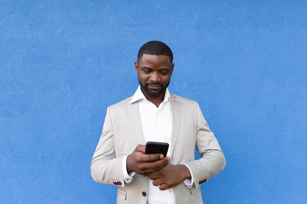 El afroamericano feliz con teléfono sobre fondo azul.