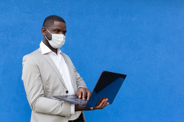 Afroamericano en una máscara protectora con un portátil en la mano