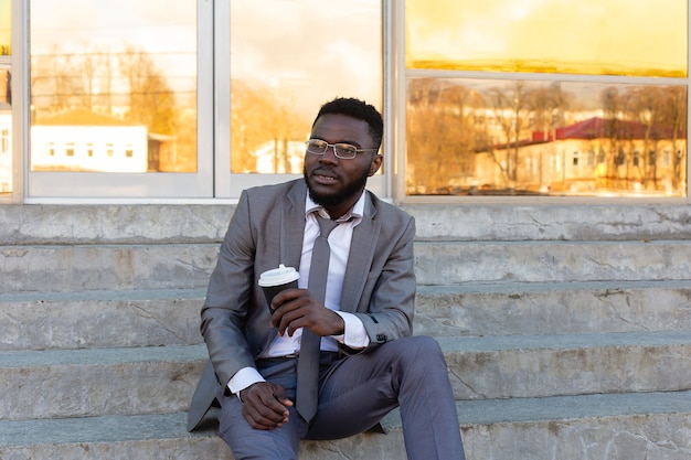 Un afroamericano se sienta en las escaleras con un café y un teléfono.