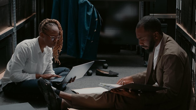 Afroamericanos trabajando en un caso de investigación policial con pruebas forenses y pistas a bordo. Equipo de inspectores que examinan fotos y verifican los antecedentes de los sospechosos. Disparo de trípode.