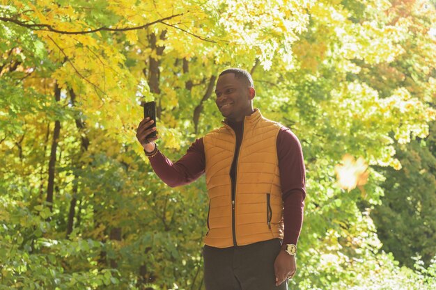Afroamerikaner, der ein Selbstporträt mit einem Smartphone im Herbstparkkopierraum macht Glückliche Menschen Saison und neues Normalitätskonzept