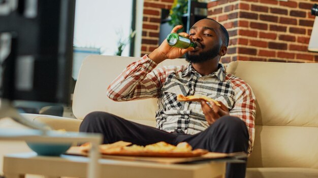 Foto afroamerikaner, der im fernsehen pizza isst und im wohnzimmer lacht handschuss.