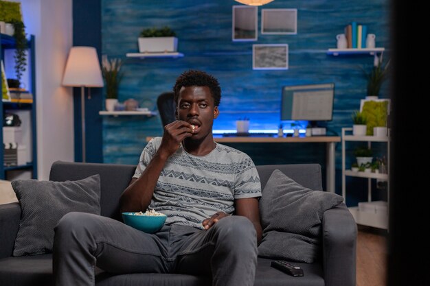 Afroamerikaner, der sich auf dem Sofa einen Unterhaltungsfilm im Fernsehen ansieht