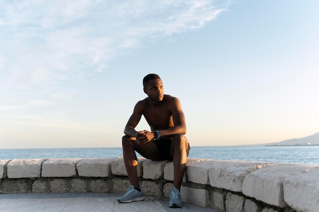Afroamerikaner, der wegschaut, während er am Meer sitzt und die Aussicht genießt