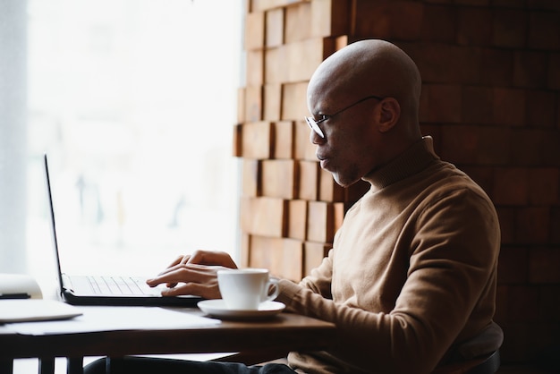 Afroamerikaner-Geschäftsmann mit Laptop in einem Café