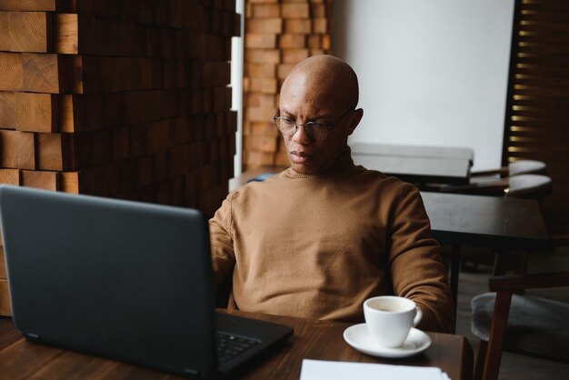 Afroamerikaner-Geschäftsmann mit Laptop in einem Café