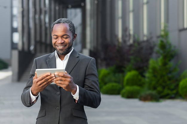 Afroamerikaner im Business-Anzug außerhalb des Bürogebäudes, der sich Online-Videos mit der App ansieht