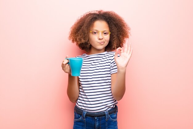 Afroamerikaner kleines Mädchen gegen flache Wand mit einer Kaffeetasse