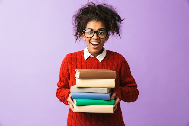 Afroamerikaner lächelndes Mädchen in der Schuluniform, die Bündel Bücher hält, lokalisiert