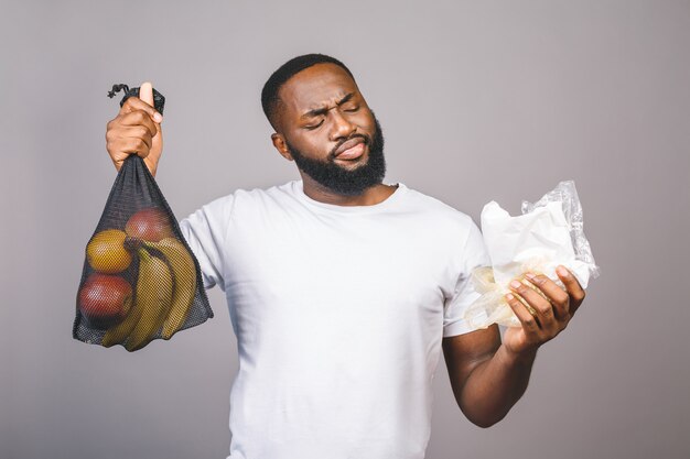 Afroamerikaner schwarze Männer hält Netztasche mit Produkten ohne Plastikverpackung über grauem Hintergrund isoliert.