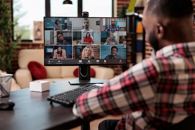 Afroamerikaner spricht über Videoanrufe mit Bürokollegen und nutzt Online-Telekonferenz-Chat mit Webcam und Computer. Remote-Arbeiten mit Videokonferenzanrufen am Heimarbeitsplatz.