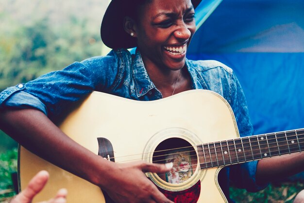 Afroamerikanerfrau, die eine Gitarre an einem Campingplatz spielt