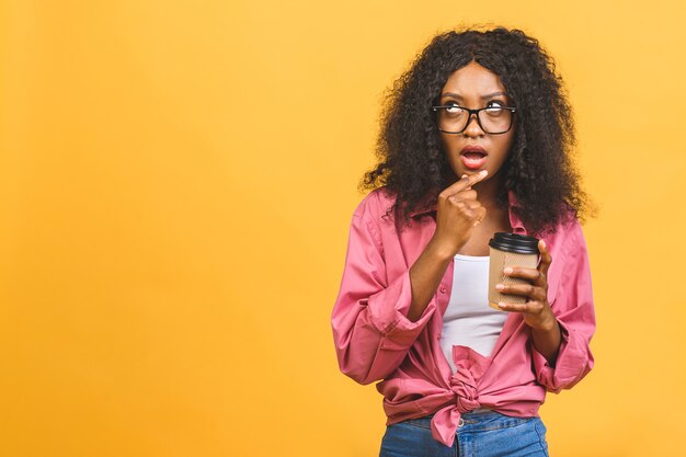 Afroamerikanerfrau mit Afro-Frisur, die beiseite schaut, während Kaffee zum Mitnehmen vom Pappbecher trinkt