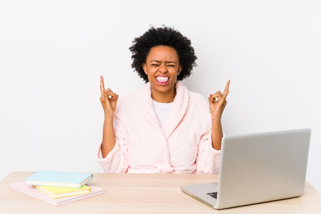 Afroamerikanerfrau mittleren Alters, die zu Hause arbeitet, lokalisiert, Rockgestik mit den Fingern zeigend