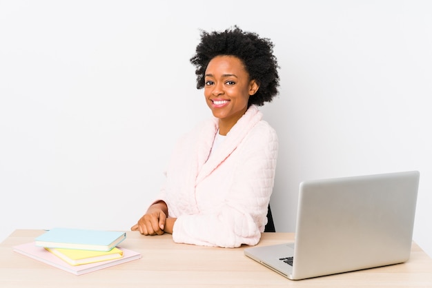 Afroamerikanerfrau mittleren Alters, die zu Hause isoliert arbeitet, sieht beiseite lächelnd, fröhlich und angenehm aus.