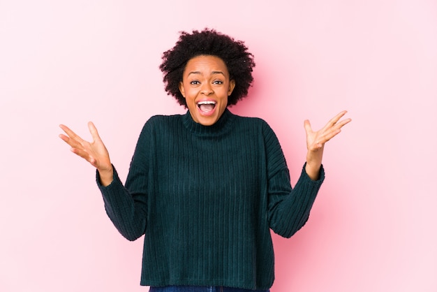 Afroamerikanerfrau mittleren Alters gegen eine rosa Wand isoliert, die einen Sieg oder Erfolg feiert, ist er überrascht und schockiert.