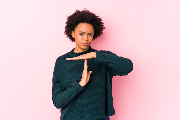 Afroamerikanerfrau mittleren Alters gegen eine rosa Wand lokalisiert, die eine Zeitüberschreitungsgeste zeigt.