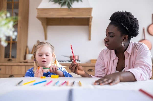 Afroamerikanerfrau und ein Mädchen, das Farben und Zeichnen lernt