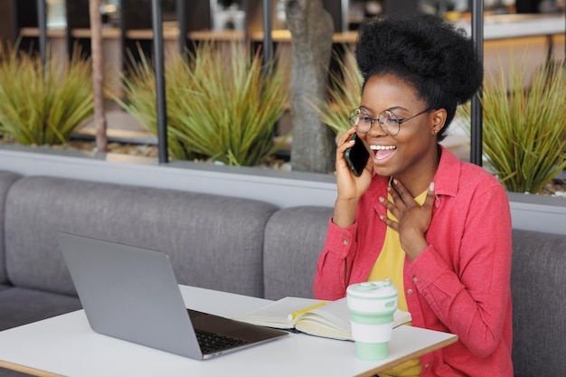 Afroamerikanerin arbeitet an einem Laptop und telefoniert mit einer glücklichen Jahrtausendfrau