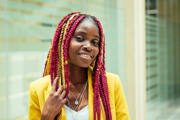 Afroamerikanerin der kreativen Stylistin mit langen Afro-Zöpfen des Kanekalon-Haars in einer gelben Jacke. schöne Kleidung Designer Schneiderin posiert im Handwerksarbeitsplatz Büro.