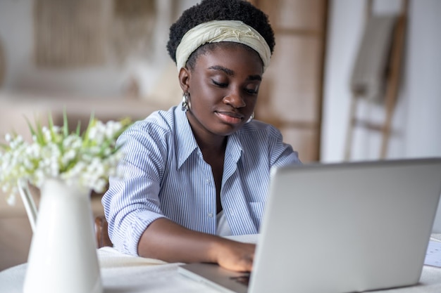 Afroamerikanerin, die am Tisch sitzt und an einem Laptop arbeitet