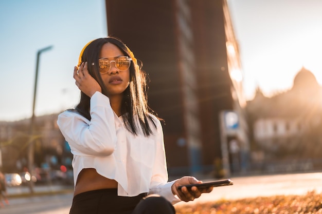 Afroamerikanerin, die bei Sonnenuntergang in der Stadt Online-Musik Musik mit Kopfhörern hört