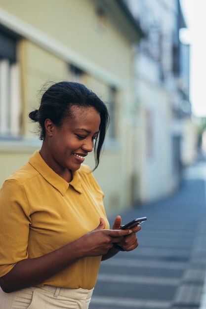 Afroamerikanerin, die ein Smartphone benutzt, während sie in der Stadt spazieren geht