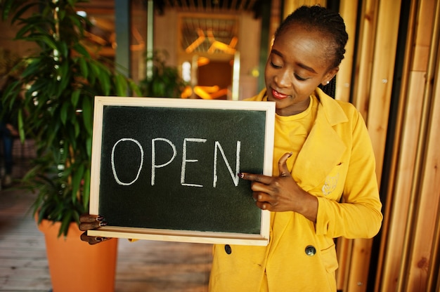 Afroamerikanerin hält offenes Willkommensschild im modernen Café-Café bereit für den Service, Restaurant, Einzelhandelsgeschäft, Kleinunternehmer.