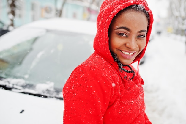 Afroamerikanerin im roten Hoodie sauberes Auto vom Schnee am Wintertag.