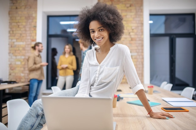 Afroamerikanerin. Lockiges Afroamerikanermädchen, das im Büro arbeitet und zufrieden schaut