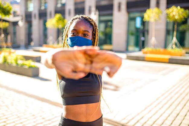 Afroamerikanerin mit langen gelben Dreadlocks-Zöpfen, die im Freien mit Maske in der Innenstadt trainieren