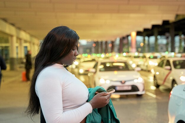 Afroamerikanerin wartet auf ihr Taxi, während sie auf ihr Handy schaut