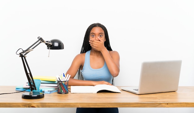 Afroamerikanerjugendlich-Studentenmädchen mit dem langen umsponnenen Haar an ihrem Arbeitsplatzbedeckungsmund mit den Händen