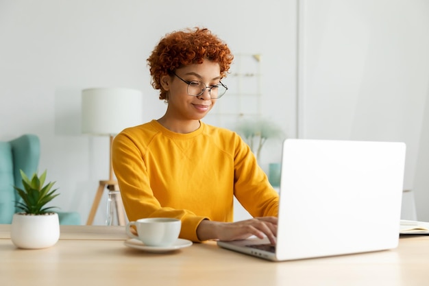 Afroamerikanermädchen, das Laptop zu Hause im Büro verwendet und Bildschirm eintippt, chattet, liest, E-Mail schreibt Junge Frau, die ein virtuelles Treffen hat, Online-Chat, Videoanrufkonferenz