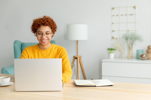 Afroamerikanermädchen, das Laptop zu Hause im Büro verwendet und Bildschirm eintippt, chattet, liest, E-Mail schreibt Junge Frau, die ein virtuelles Treffen hat, Online-Chat, Videoanrufkonferenz