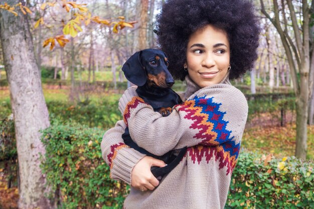 Afroamerikanermädchen, das sitzt und ihren Hund im Park im Herbst umarmt