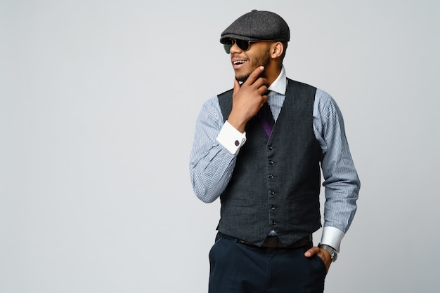 Afroamerikanermann, der Kappe, Hemd und Krawatte über graue Wand trägt
